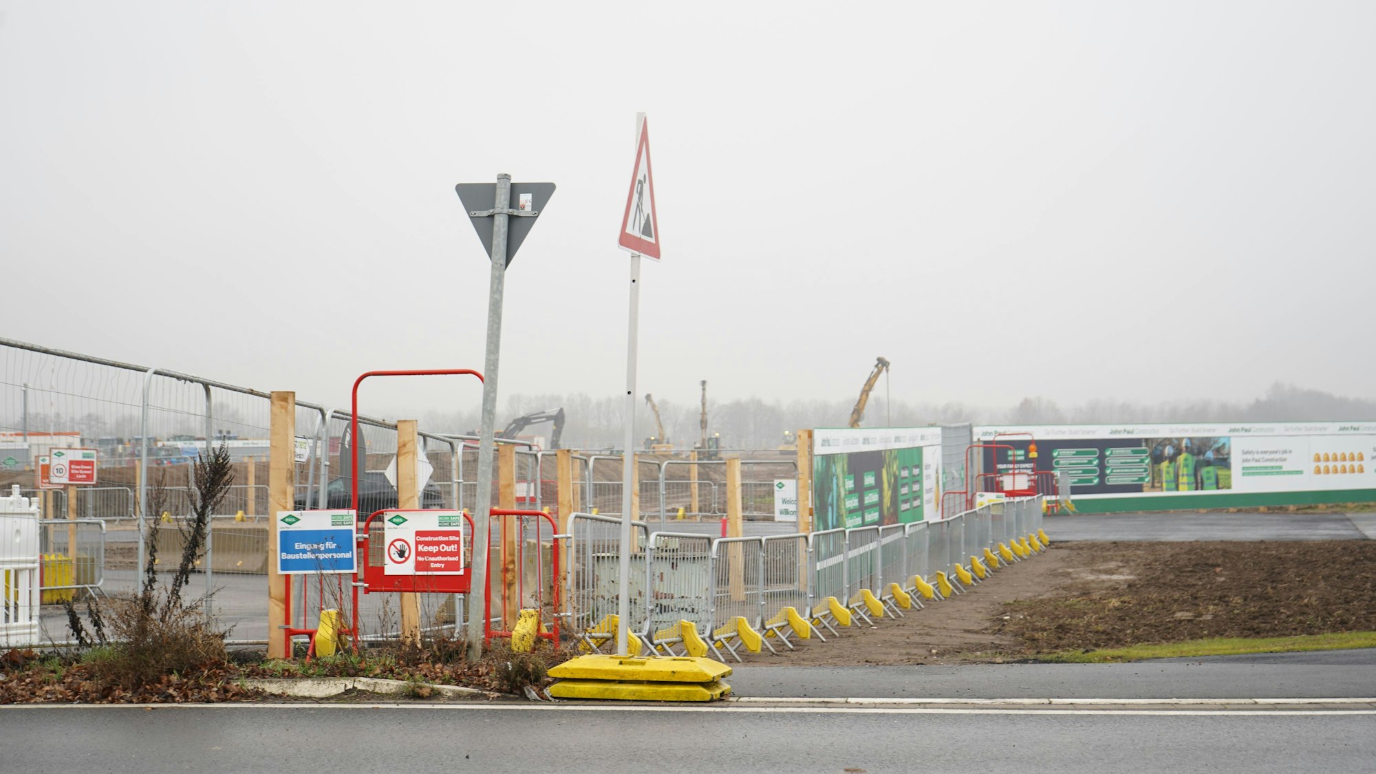Das BIld zeigt einen Bauzaun und Baustellenschilder, im Hintergrund Baufahrzeuge.