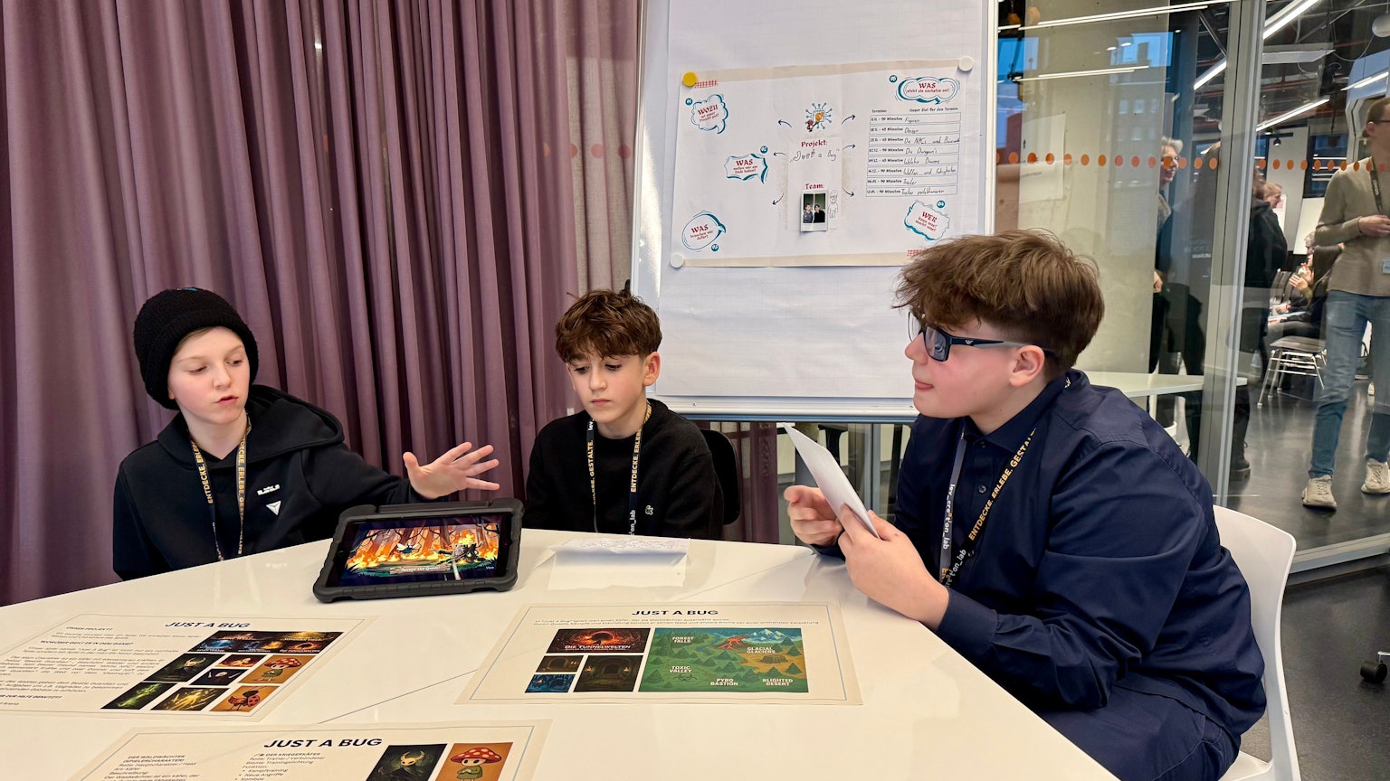 Drei Kinder, die ein Spiel mit Hilfe von Künstlicher Intelligenz entwickelt haben, sitzen an einem Tisch.