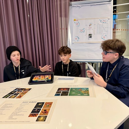 Drei Kinder, die ein Spiel mit Hilfe von Künstlicher Intelligenz entwickelt haben, sitzen an einem Tisch.