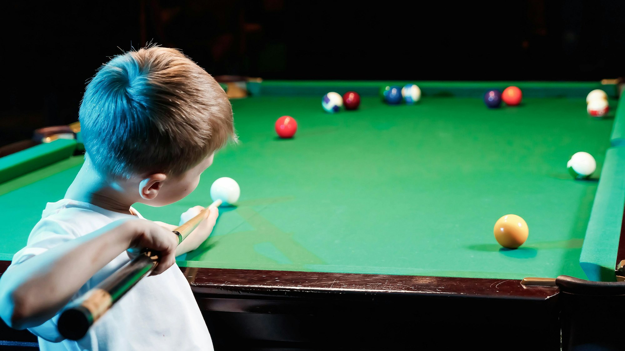 Ein Junge steht mit einem Queue an einem Billardtisch. (Symbolbild)