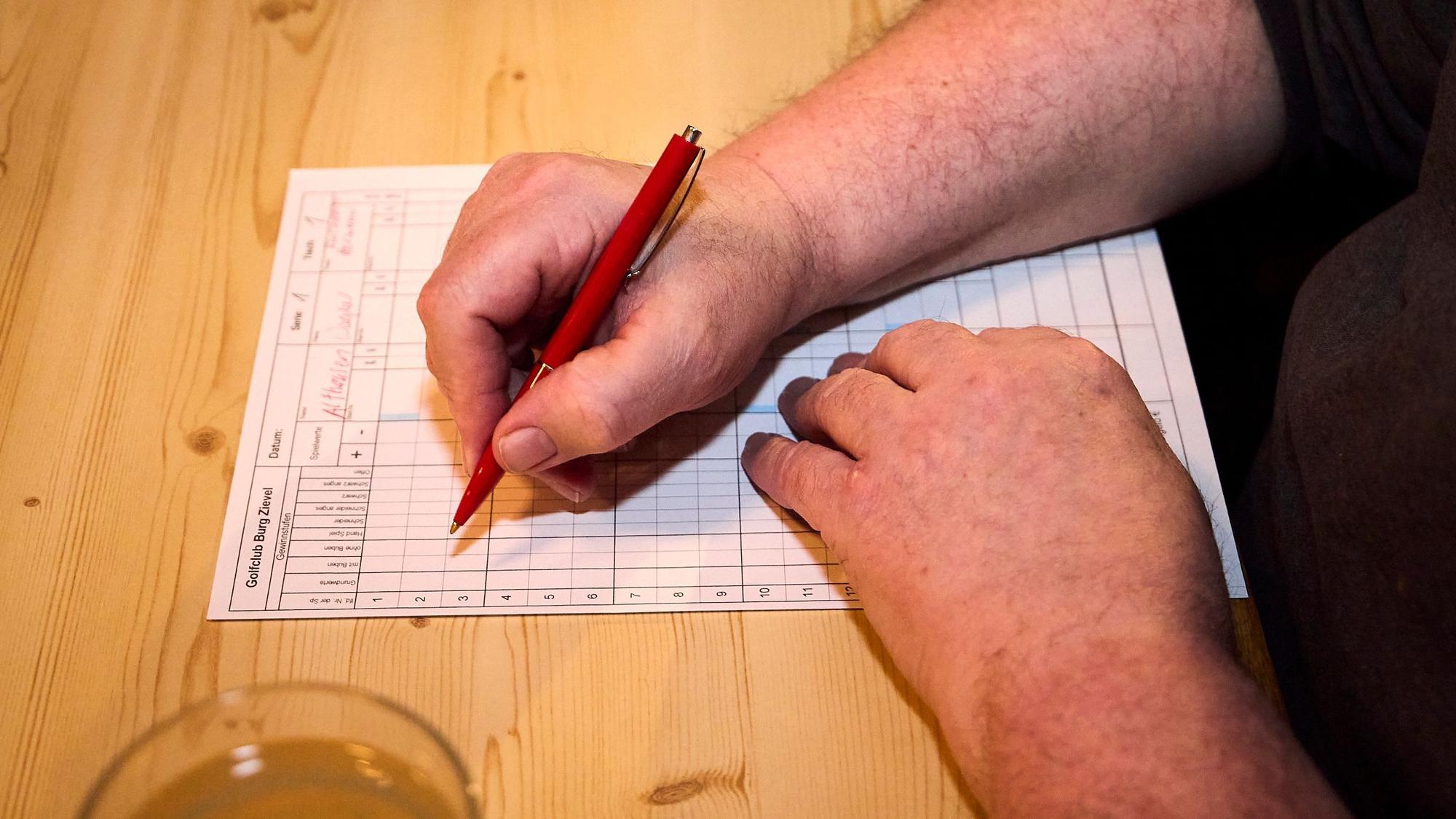 Nahaufnahme auf eine Hand, die mit einem Stift etwas auf einem Notizzettel einträgt