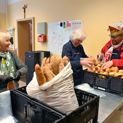 Torsten Krieg packt neben zwei älteren Damen Brötchen aus einem Korb in eine Plastiktüte.
