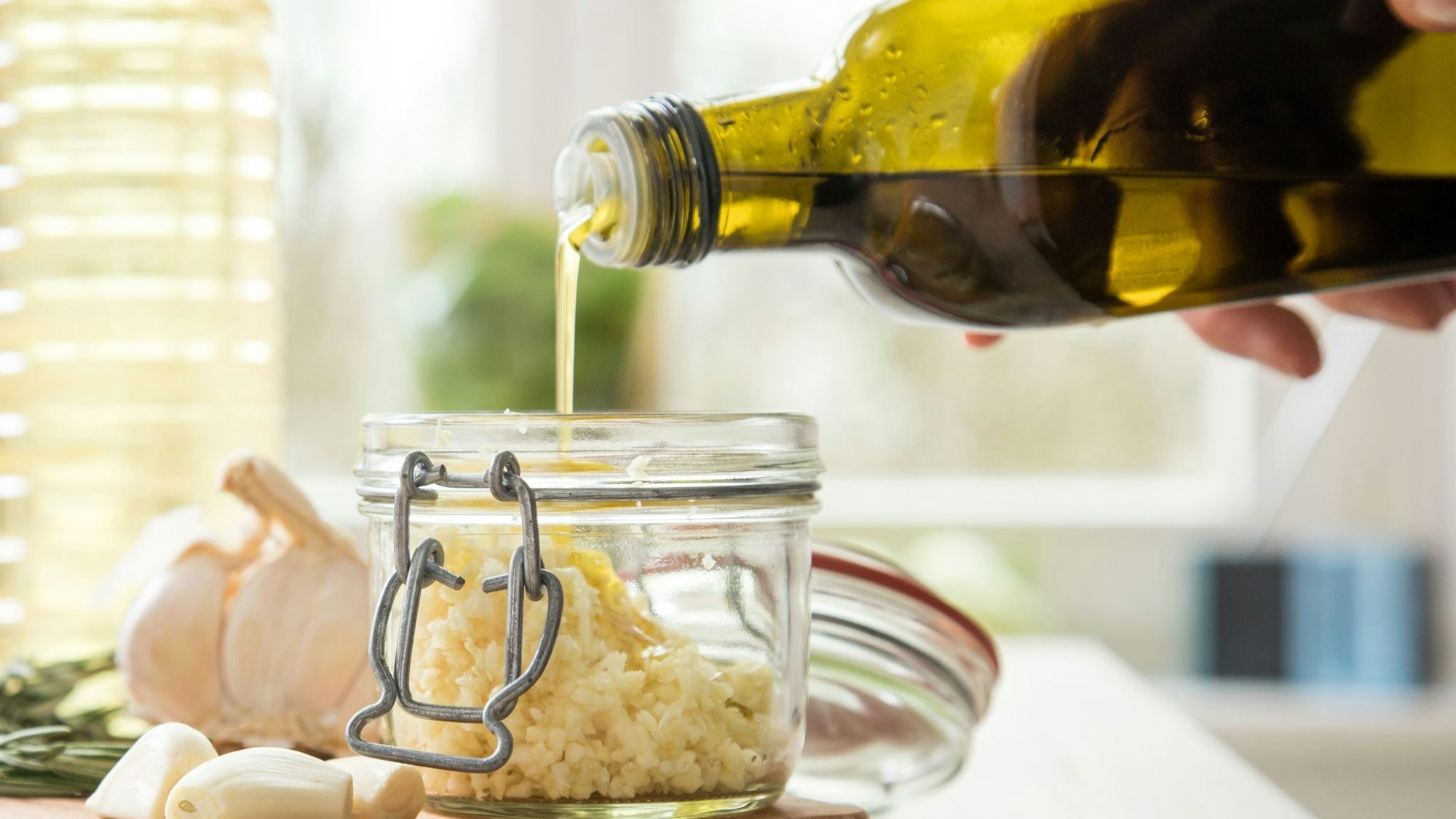 Jemand gießt Olivenöl in ein Glas mit Knoblauch.