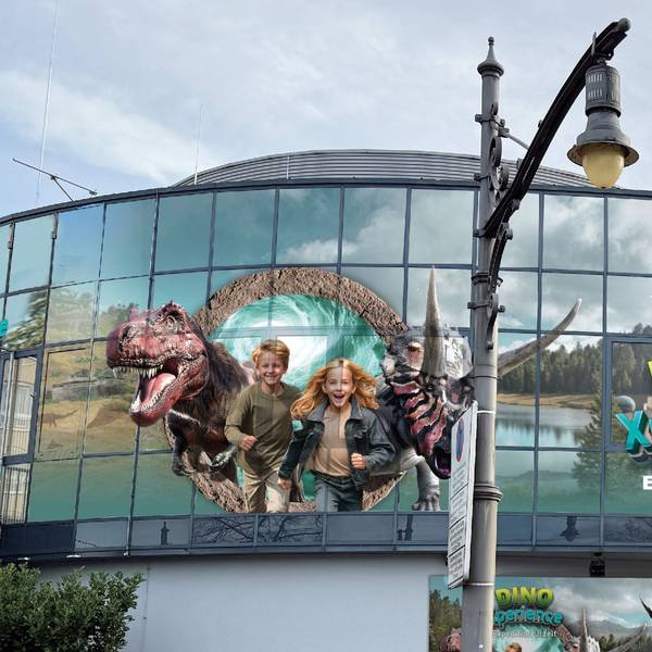 Große Darstellungen von Kindern und Dinosauriern an der Glasfassade eines Gebäudes.