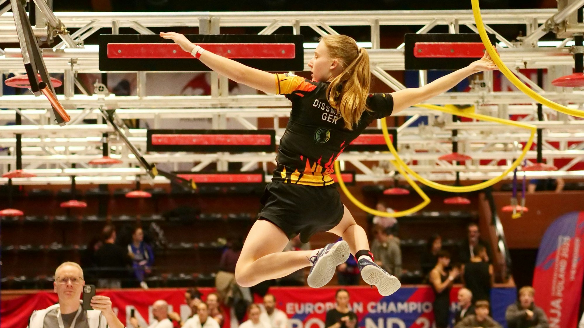 Szene aus dem Ninja-Sport, eine junge Frau hangelt durch einen Hindernisparcours.