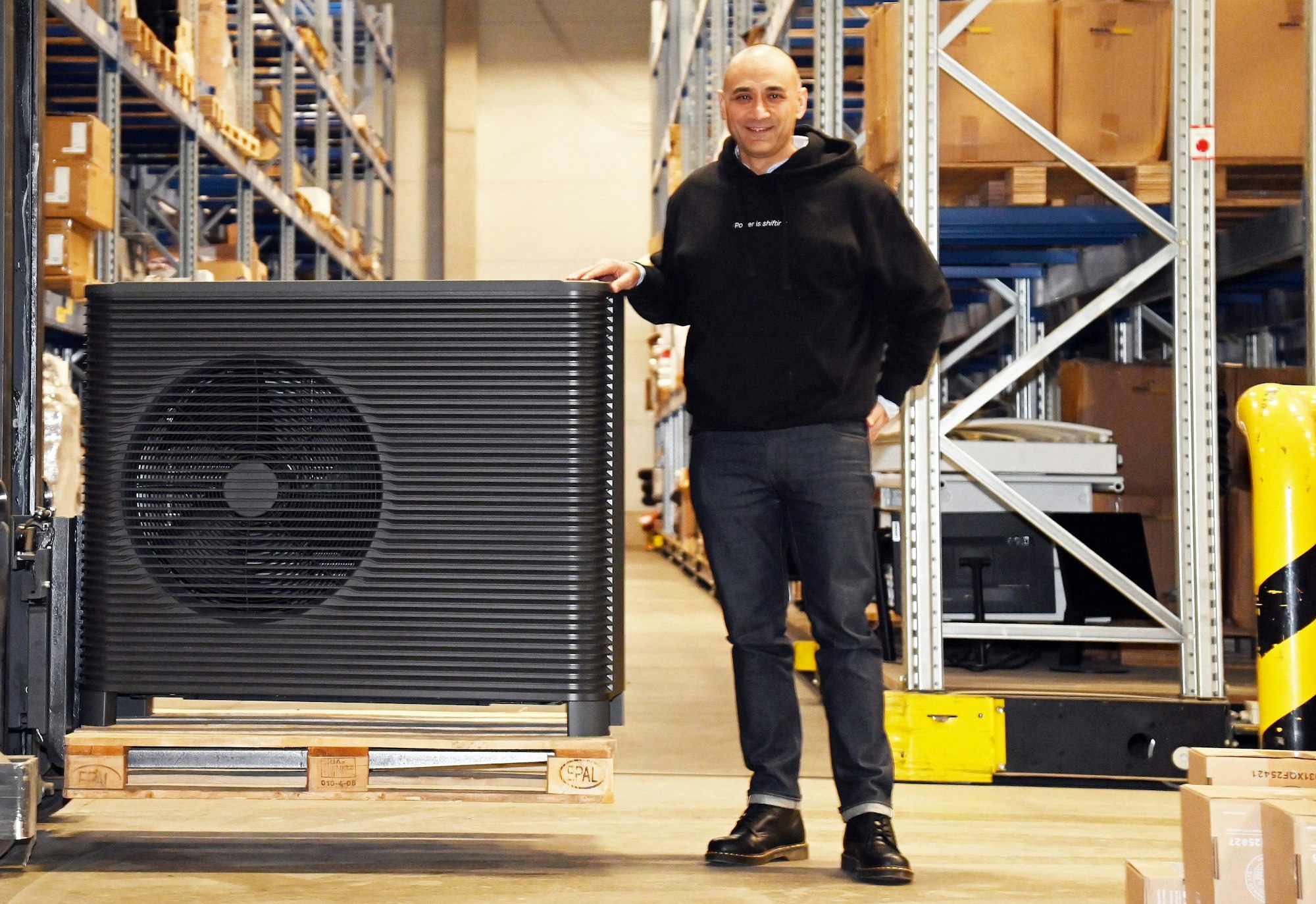 Ein Mann in Kapuzenpulli und Jeans steht neben einer Wärmepumpe.