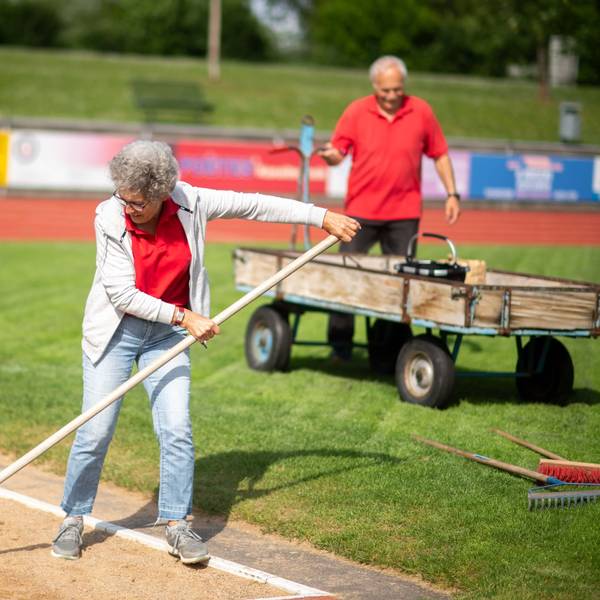 Bei einem Leichtathletik-Wettkampf helfen ein Mann (im Hintergrund) und eine Frau bei der Organisation.