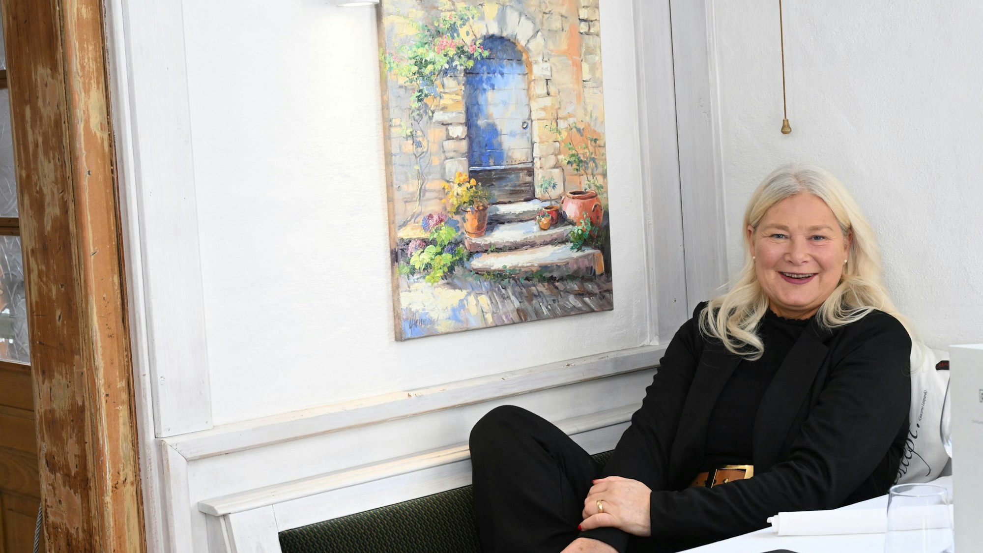 Eine Frau schaut lächelnd in die Kamera, während sie zurückgelehnt in einem Stuhl sitzt.