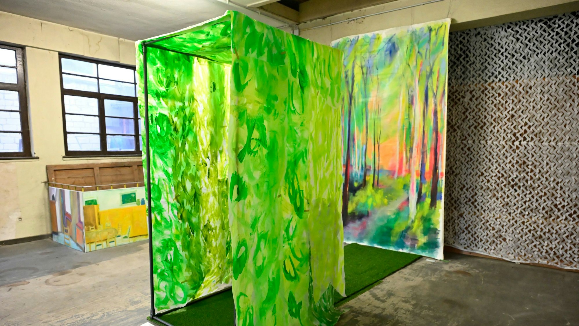 Ein Kunstwerk besteht aus einem grünen Durchgang mit Kunstrasen, der auf ein Gemälde eines Waldes hinführt.