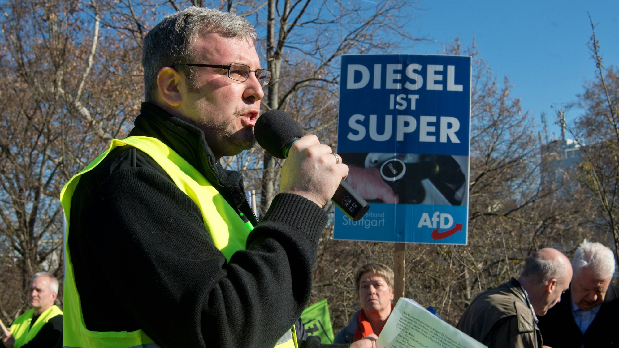 Oliver Hilburger hält auf einer AfD-Demonstartion eine Rede. Im Hintergrund halten andere Demonstranten ein AfD-Wahlplakat mit dem Slogan "Diesel ist super".