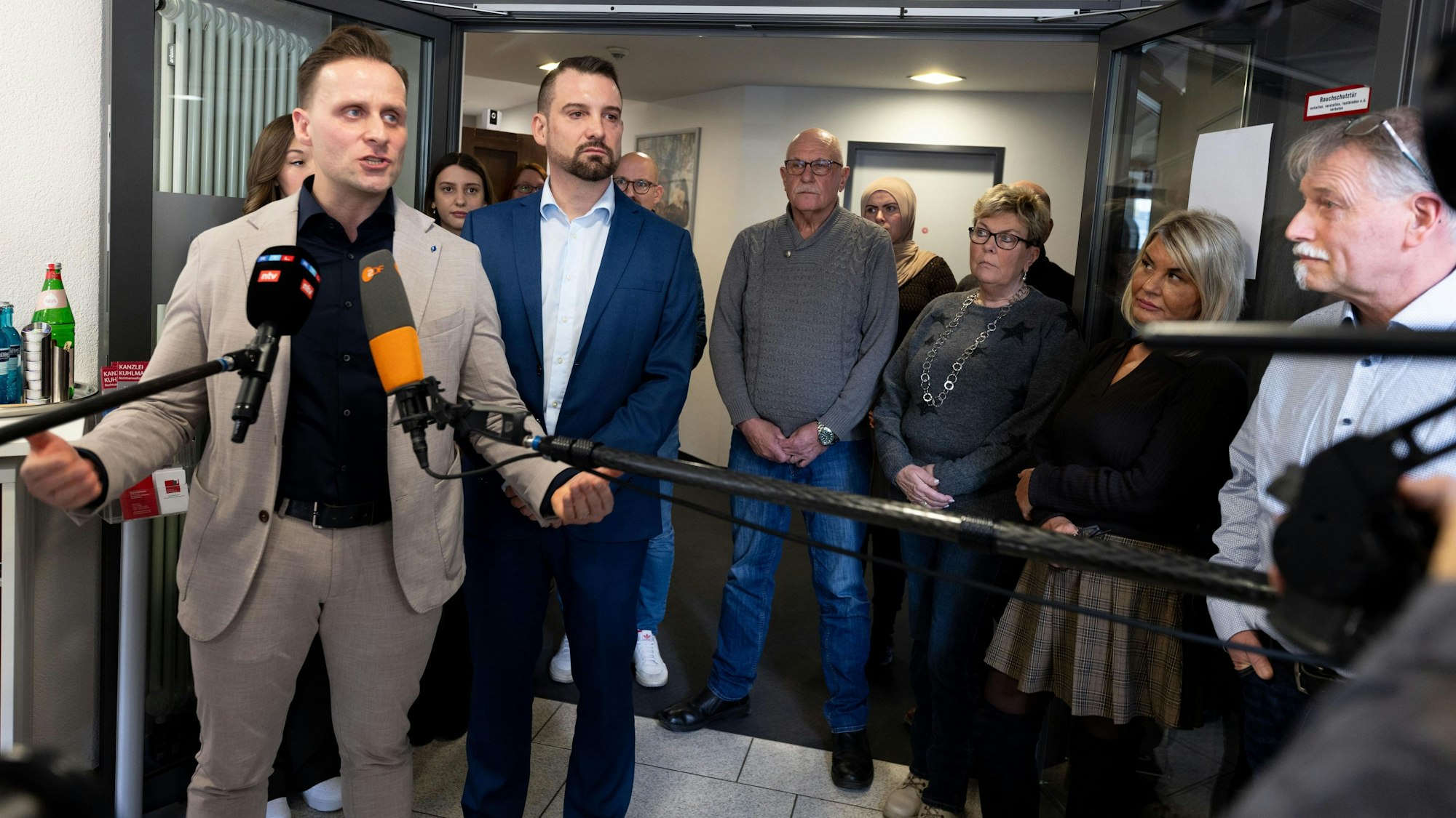 Rechtsanwalt Daniel Kuhlmann (2.v.l.) spricht gemeinsam mit den bei dem Sparkassenraub in Gelsenkirchen geschädigten Daniel Orijan (l) und Joachim Alfred Wagner (r) vor seiner Kanzlei zu Journalisten, im Hintergrund stehen weitere Geschädigte.