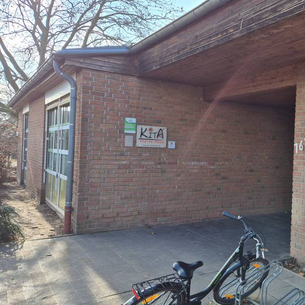 Das Bild zeigt den Eingang zur Kita. Vorne parkt ein Fahrrad an einem Ständer.