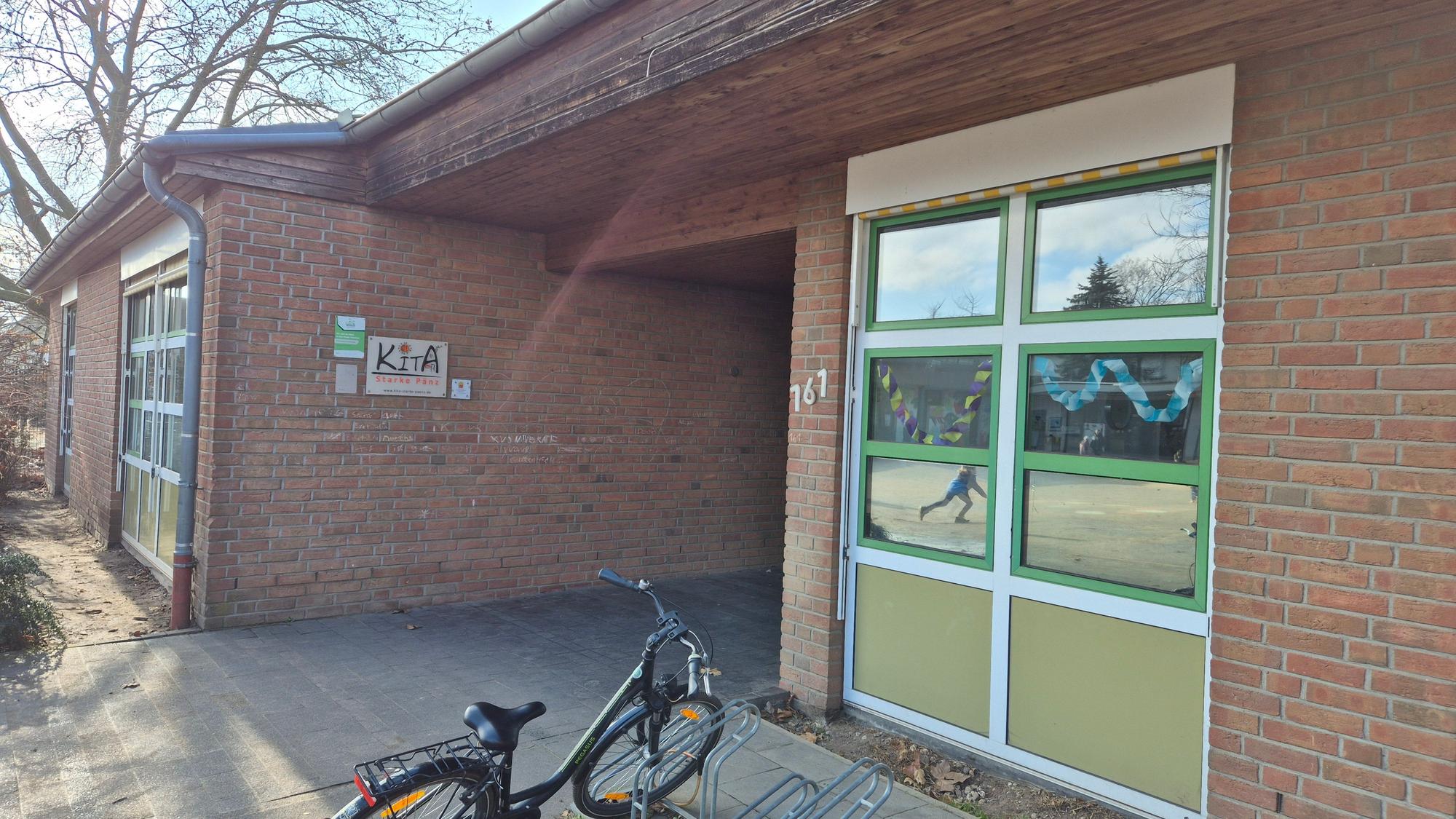 Das Bild zeigt den Eingang zur Kita. Vorne parkt ein Fahrrad an einem Ständer.
