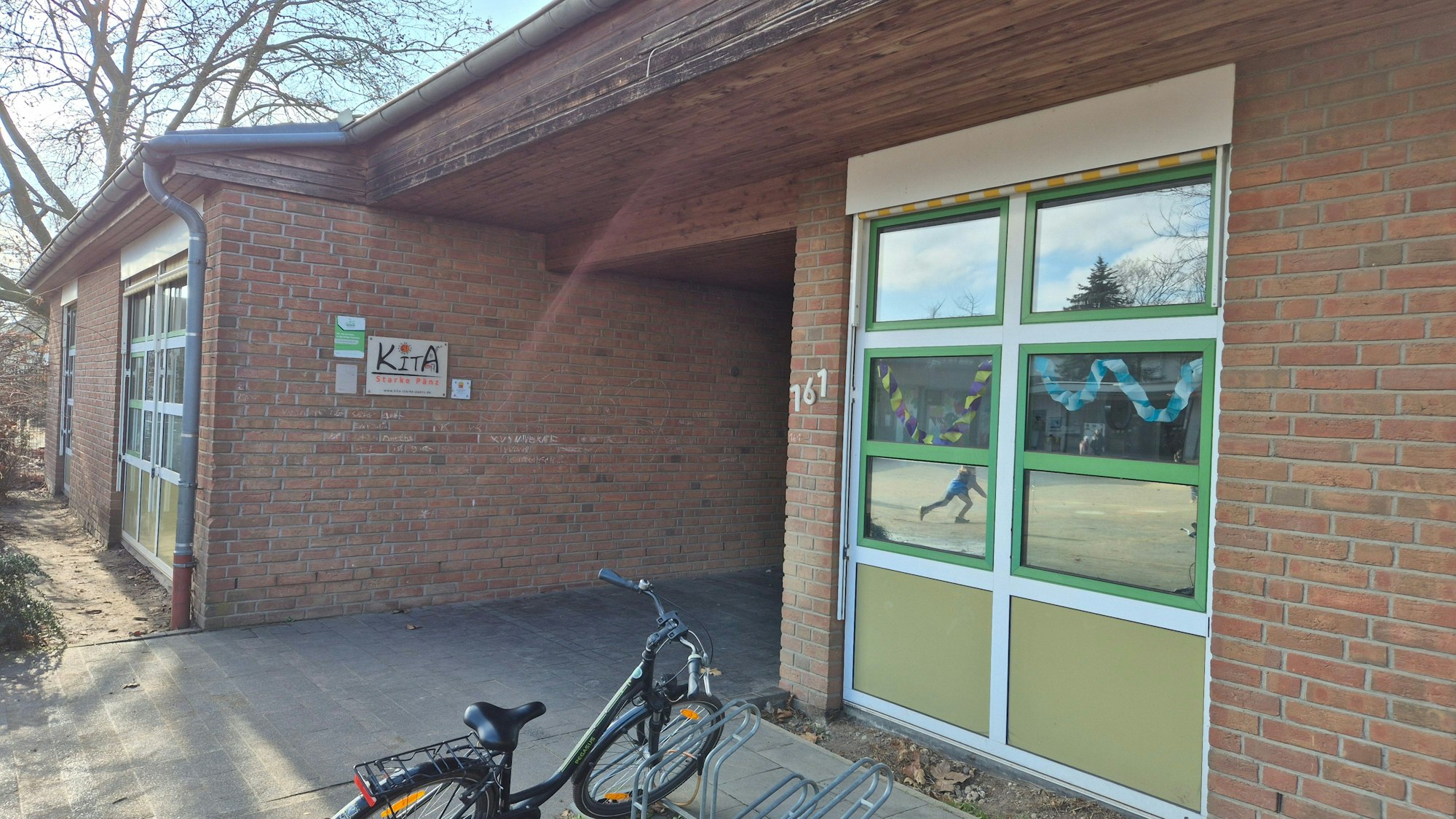 Das Bild zeigt den Eingang zur Kita. Vorne parkt ein Fahrrad an einem Ständer.