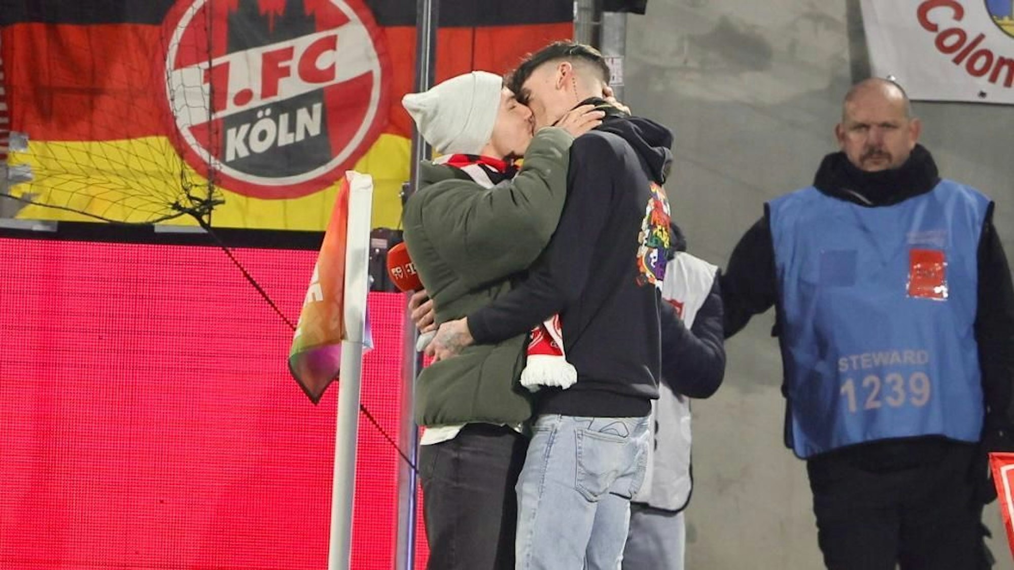 Im Stadion des 1. FC Köln küssen sich zwei Männer nach einem erfolgreichen Heiratsantrag.