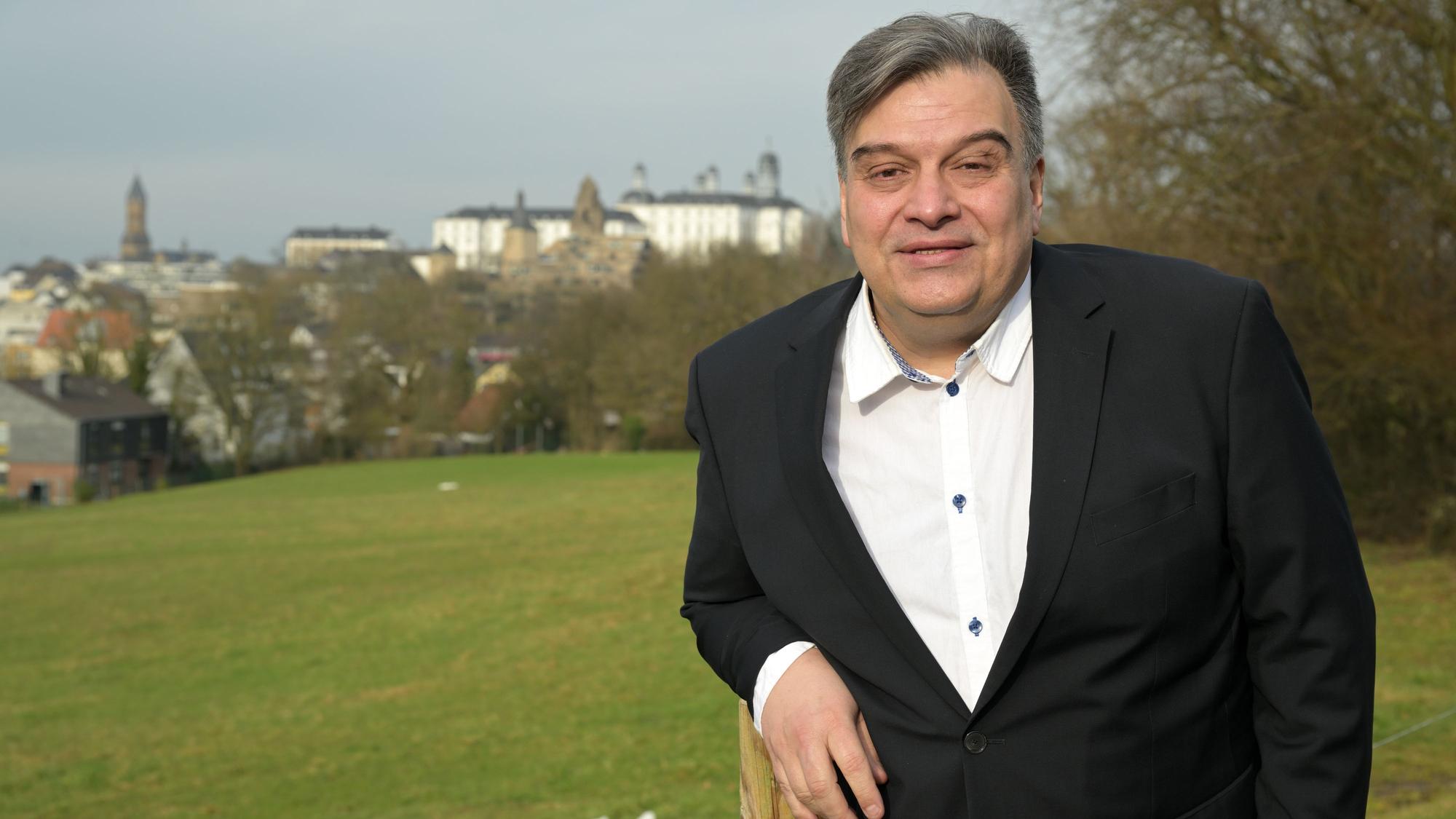 Ein Mann steht vor einer grünen Wiese, im Hintergrund sieht man das Bensberger Schloss.