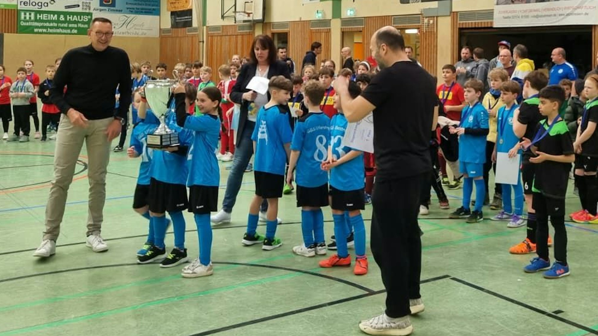 Kinder recken einen Pokal bei einem Sportturnier in die Höhe.
