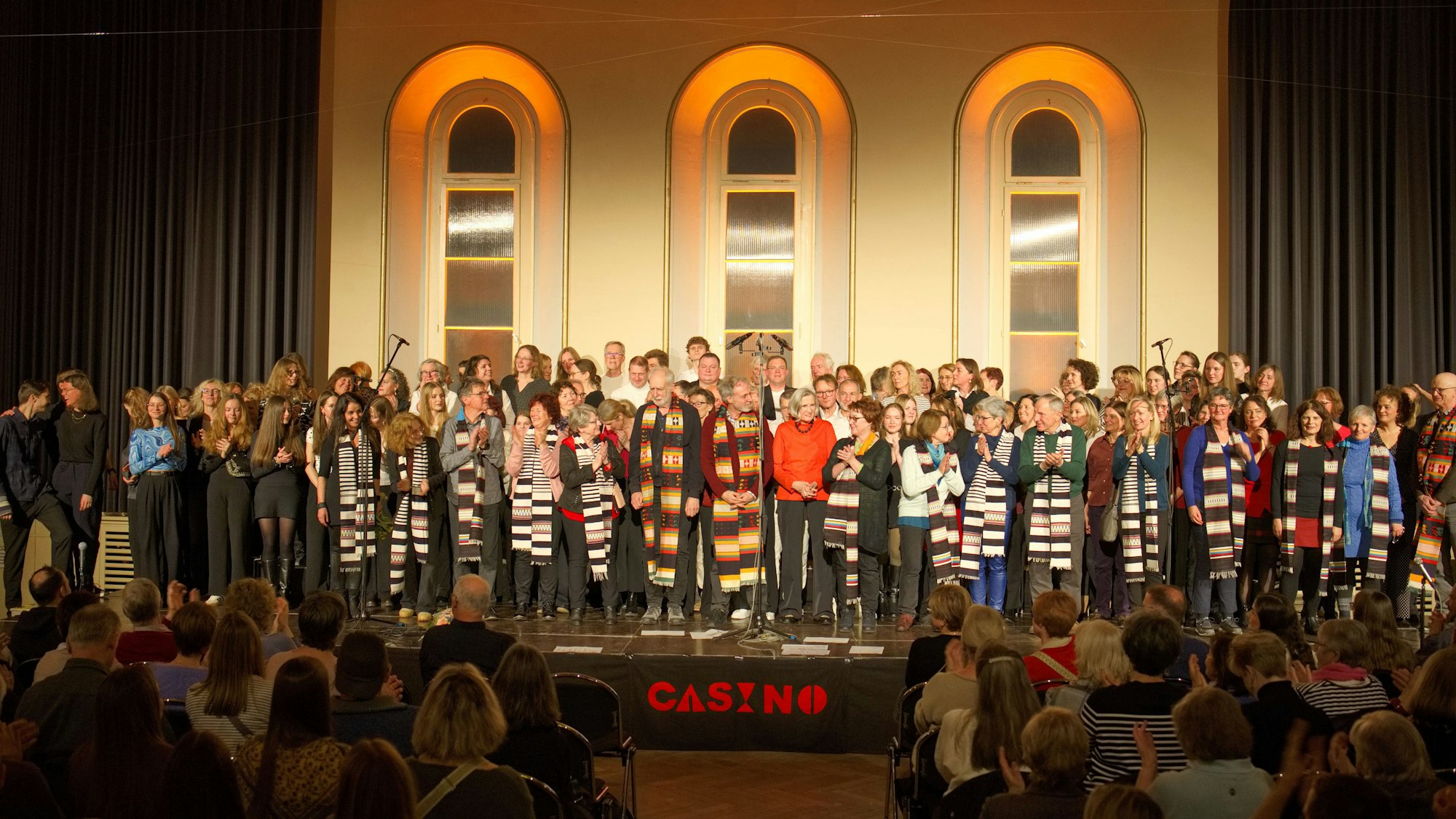 Die Mitglieder von vier Chören stehen gemeinsam auf der Bühne.