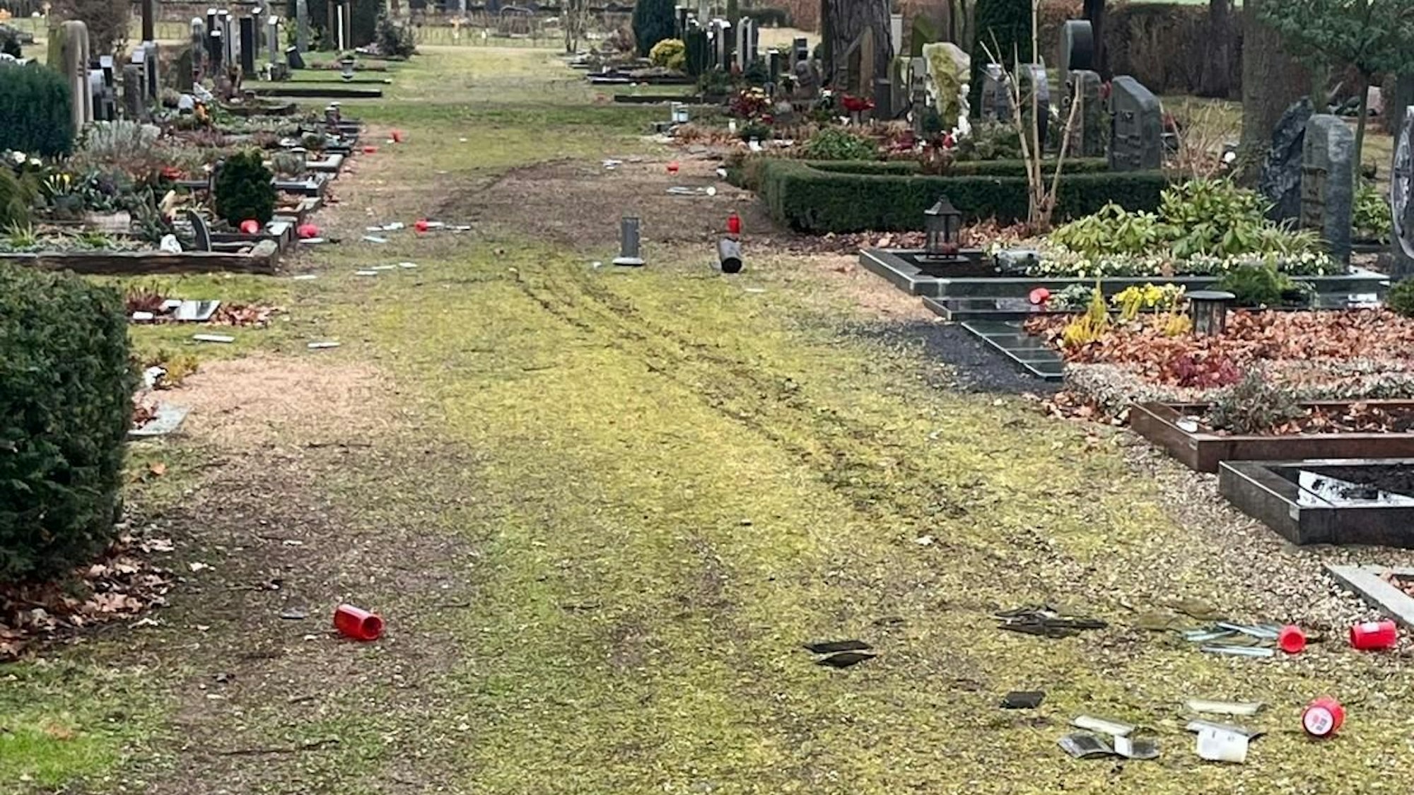 Auf einem Friedhofsweg liegen Grablichter, Glasscherben und anderer zerstörter Grabschmuck.