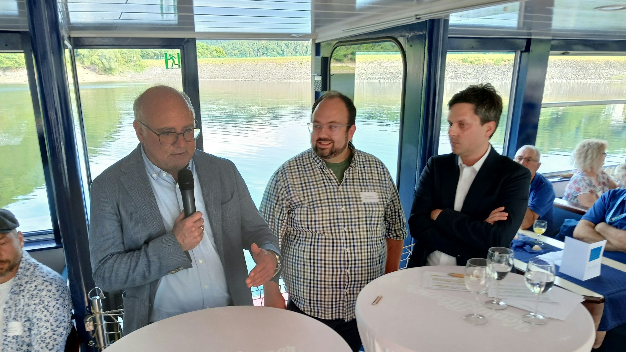 Die drei Männer stehen an Tischen nebeneinander, Jochen Weiler spricht in ein Mikrofon.