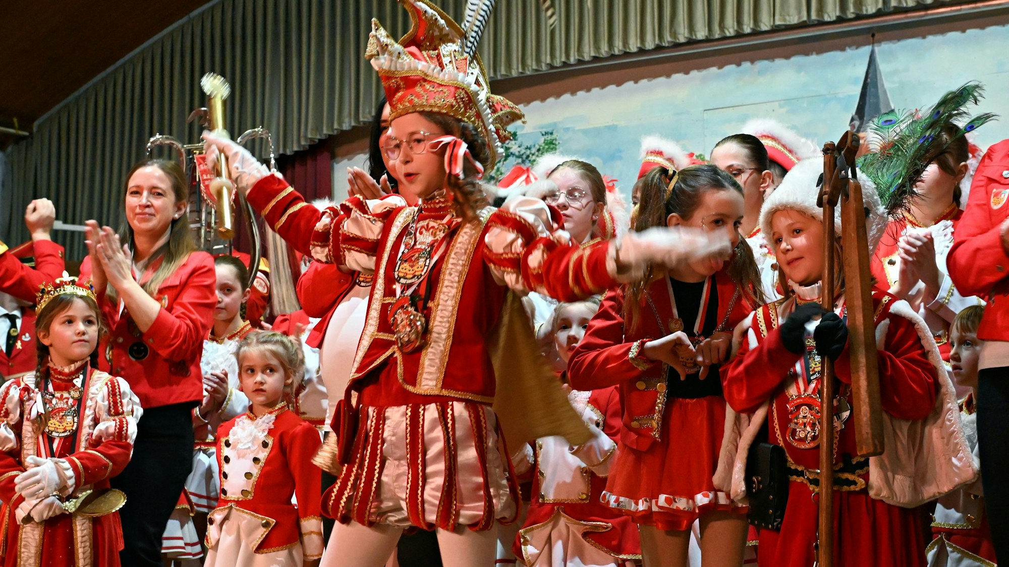 Kinder tanzen auf der Bühne, im Vordergrund ist das Kinderdreigestirn zu sehen.