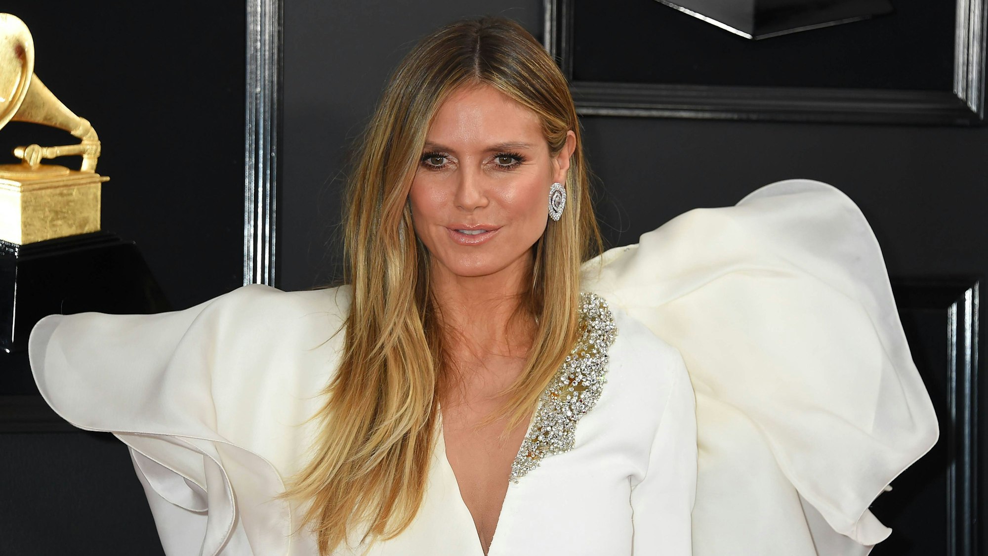 Heidi Klum in weißem Kleid mit goldener Trophäe.