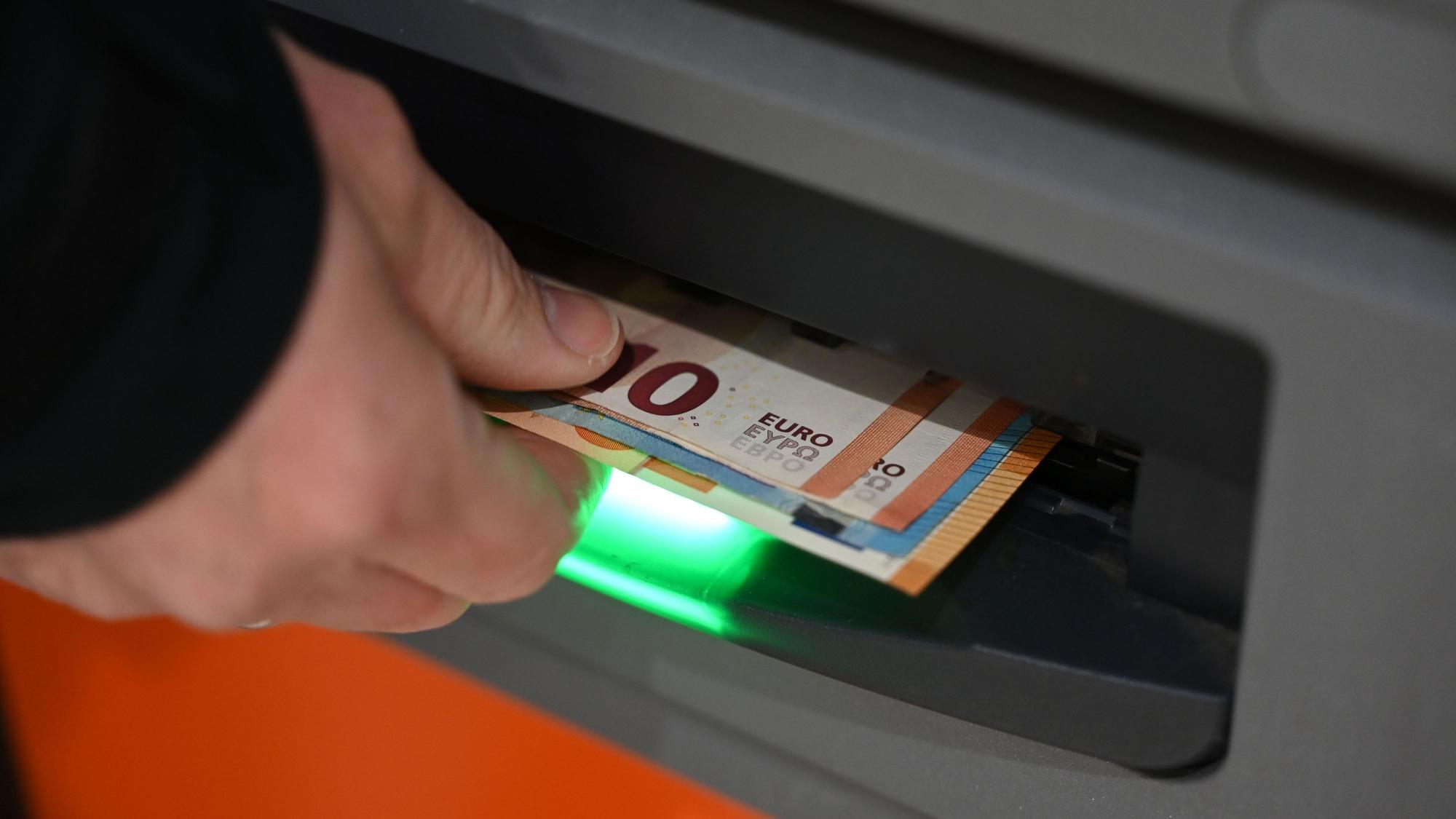 Eine Hand greift nach Banknoten, die aus dem Ausgabeschlitz des Automaten kommen.