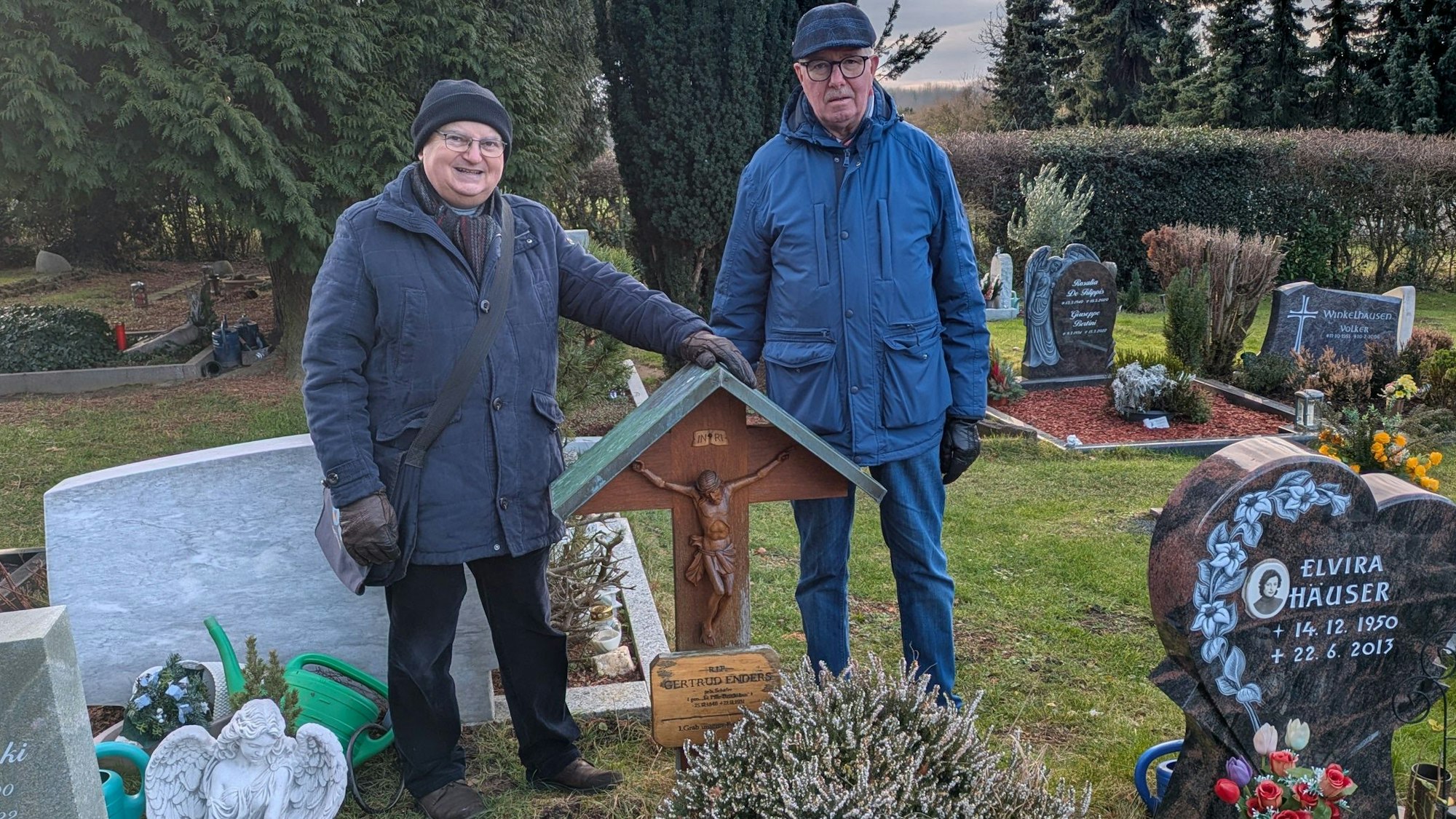 Zwei Männer stehen an einem Grab mit einem Holzkreuz.