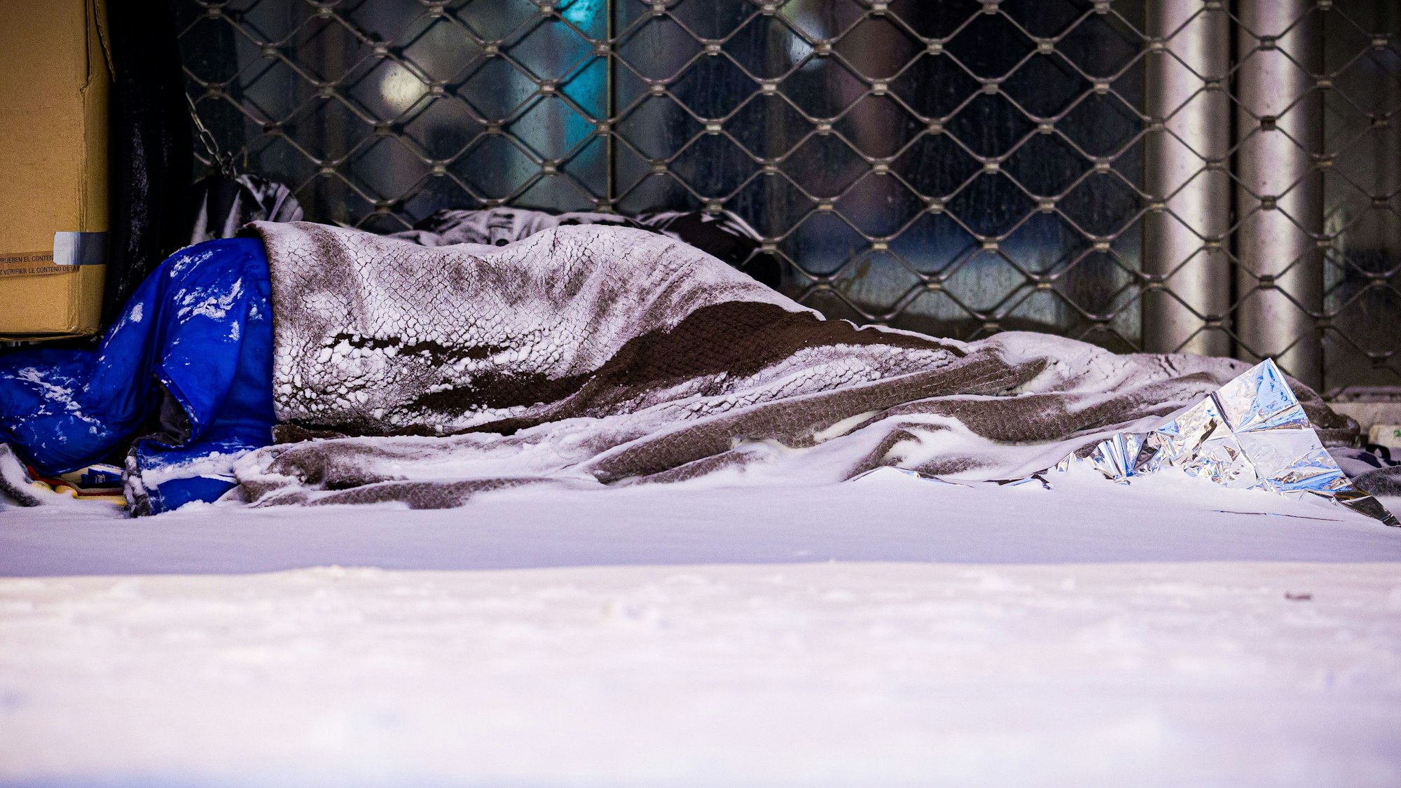 Das Foto zeigt einen Menschen, der im Schnee auf der Straße schläft.