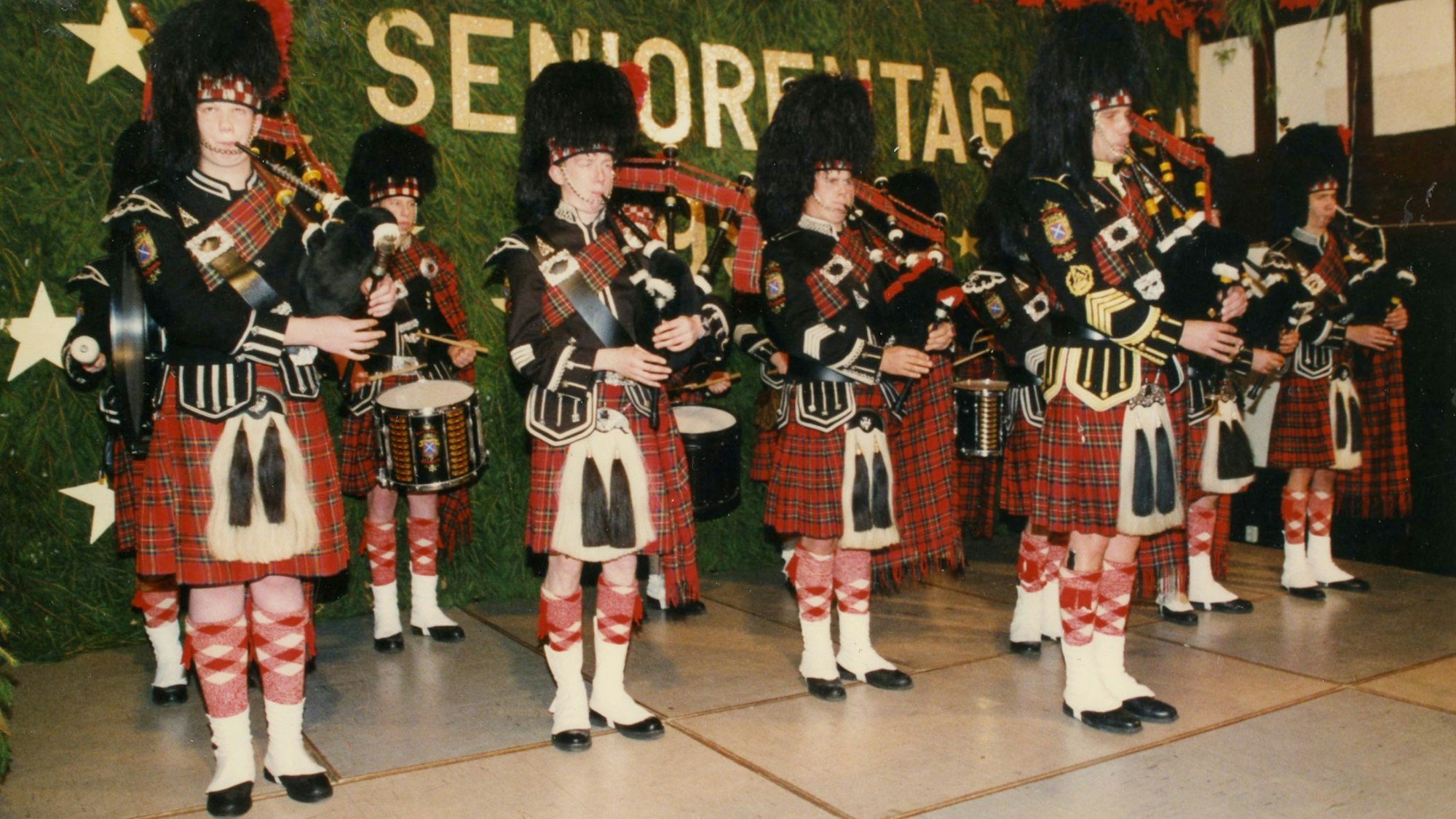 Männer im Schottenrock mit Dudelsäcken stehen auf einer Bühne, im Hintergrund ist der Schriftzug "Seniorentag" zu sehen.