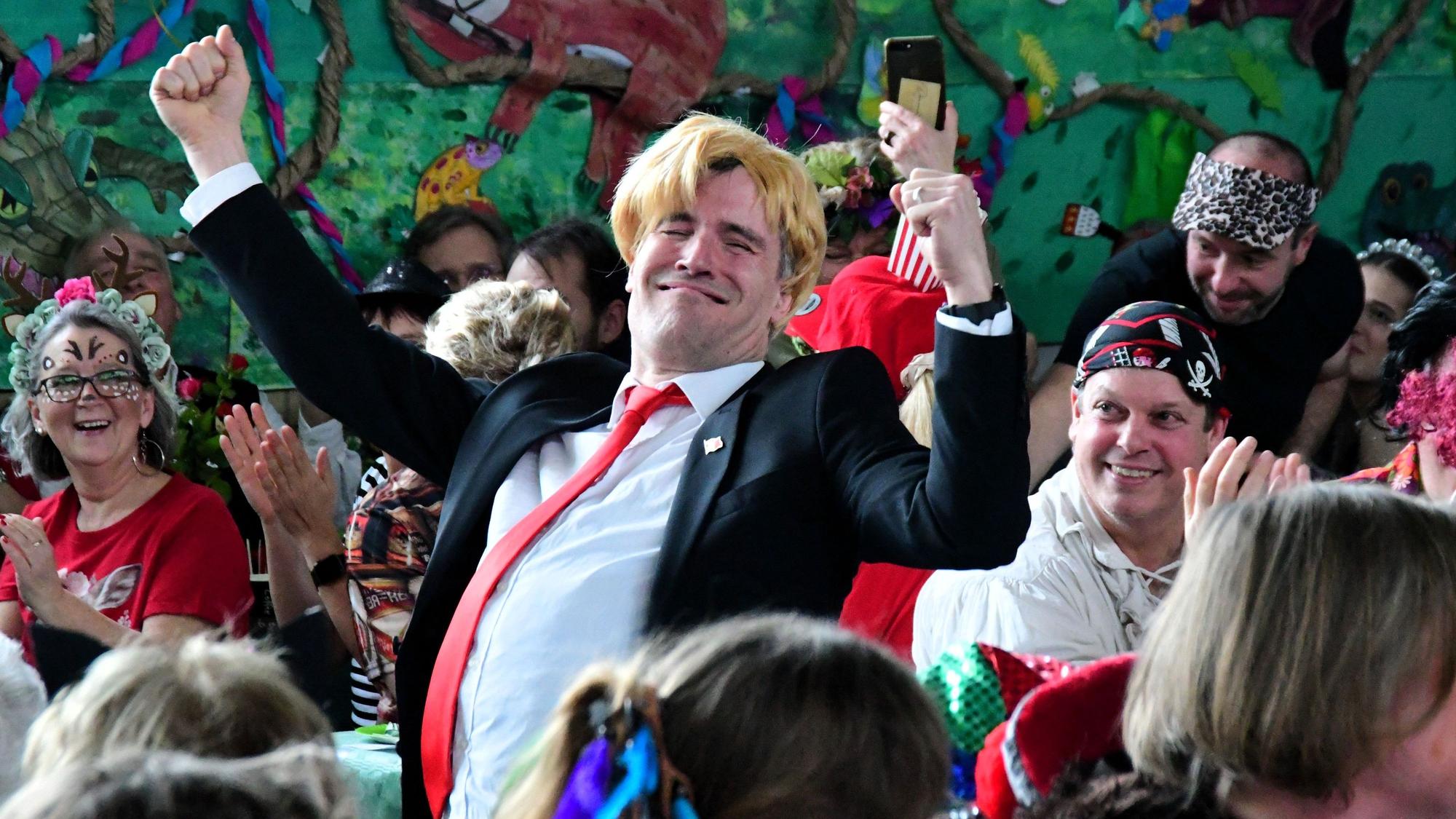 Ein als Donald Trump verkleideter Mann steht in Angeberpose zwischen den Besuchern.