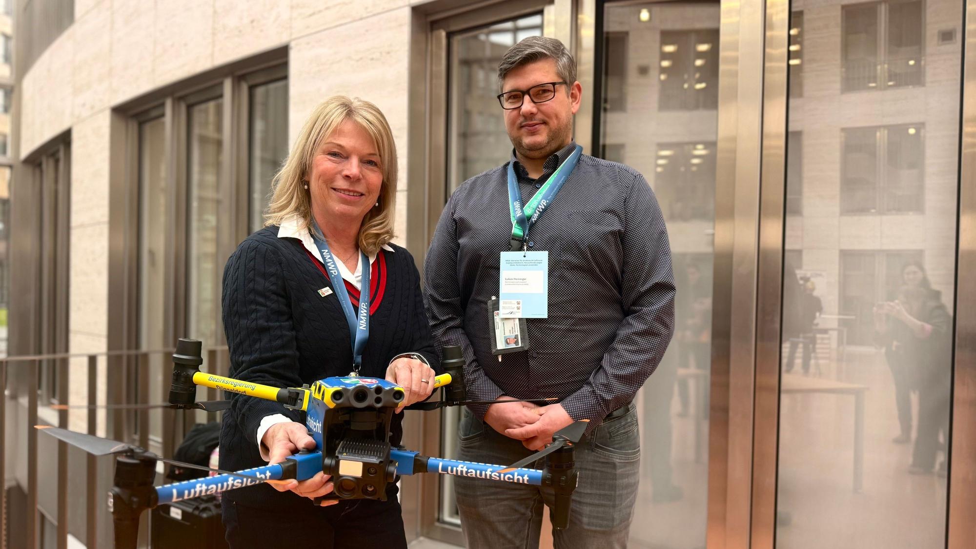 Petra Eilhard und Lukas Heininger halten eine kleine Drohner in Polizei-gelb und -blau in der Hand, auf der „Luftaufsicht“ steht.