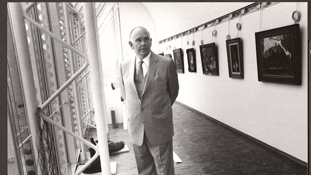 Peter Ludwig steht zwischen einer Fensterfront und einer Wand mit Gemälden.