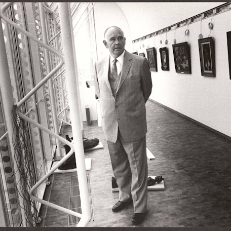 Peter Ludwig steht zwischen einer Fensterfront und einer Wand mit Gemälden.