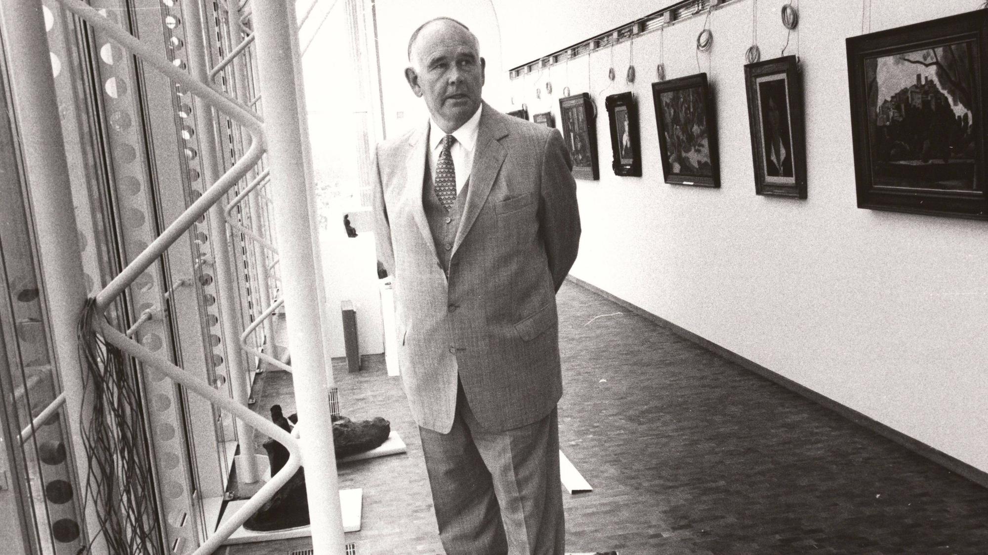 Peter Ludwig steht zwischen einer Fensterfront und einer Wand mit Gemälden.