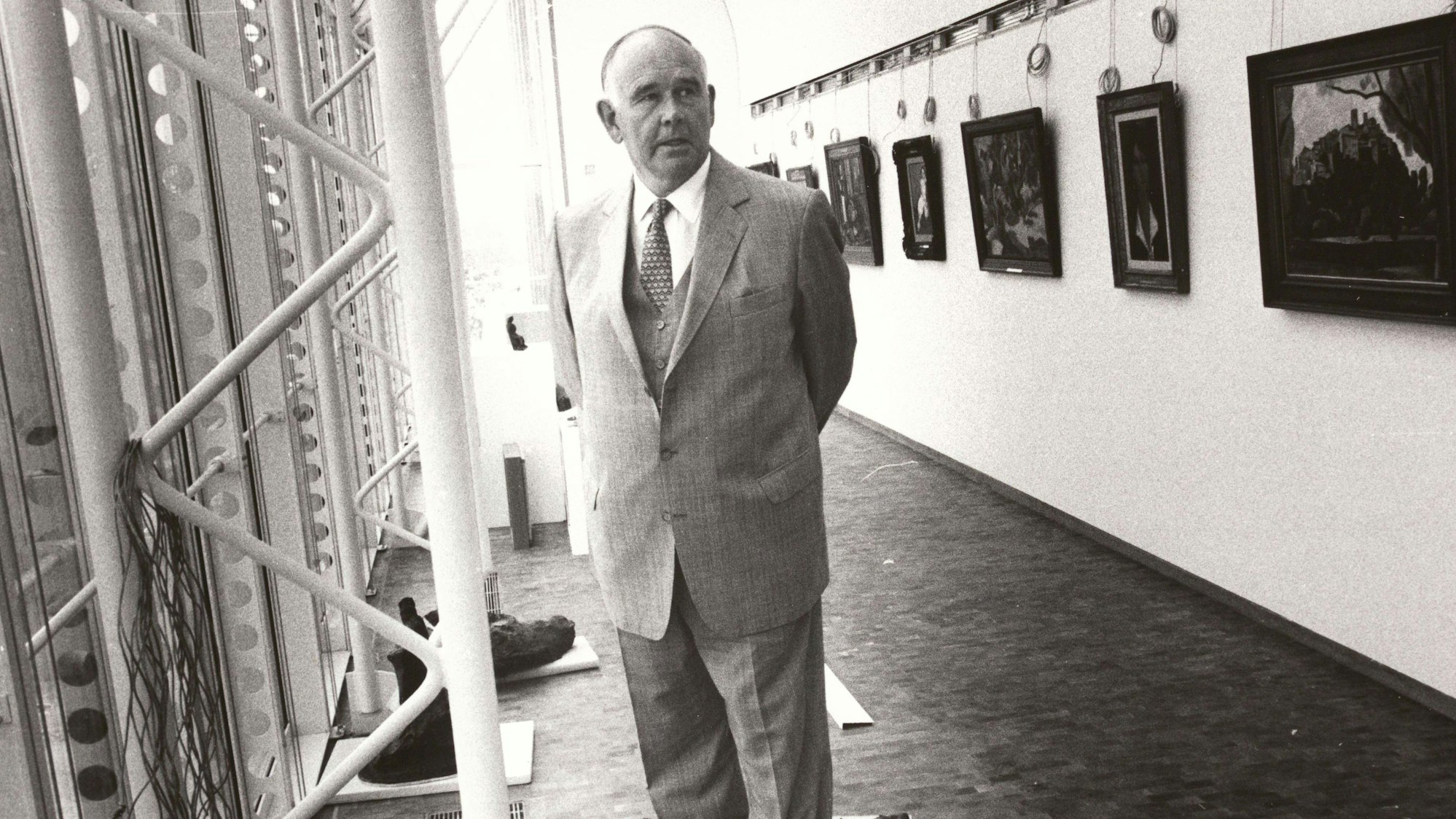 Peter Ludwig steht zwischen einer Fensterfront und einer Wand mit Gemälden.