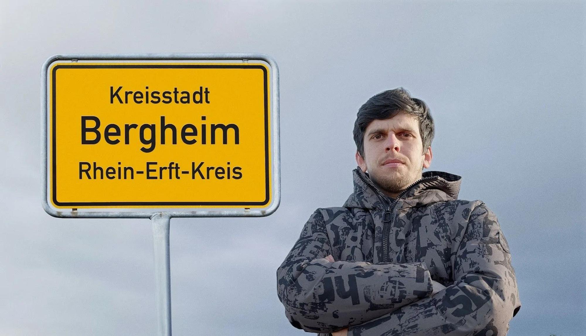 Auf dem Foto steht ein Mann mit verschränkten Armen vor einem Ortsschild der Stadt Bergheim.