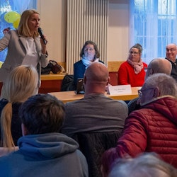 Foto einer Frau, die vor einer Bürgerversammlung spricht.