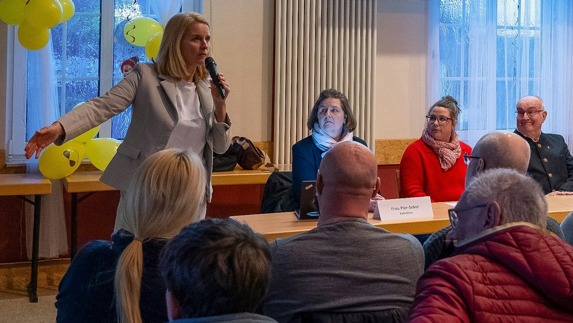 Foto einer Frau, die vor einer Bürgerversammlung spricht.