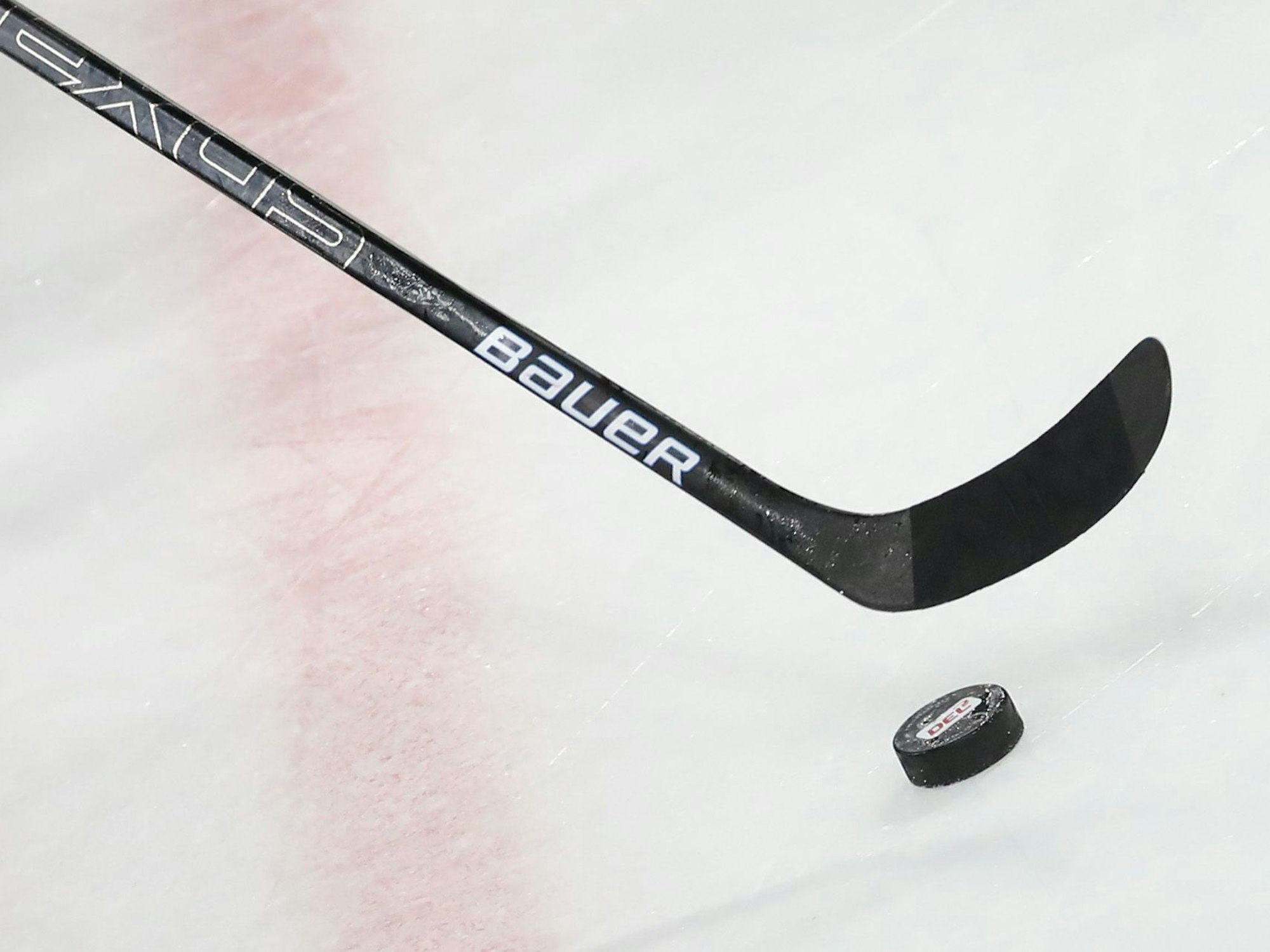 Ein Puck liegt vor einem Schläger im Spiel auf dem Eis.