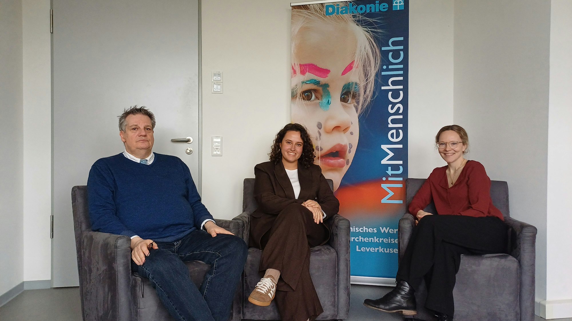 Ein Mann und zwei Frauen sitzen nebeneinander in Sesseln.