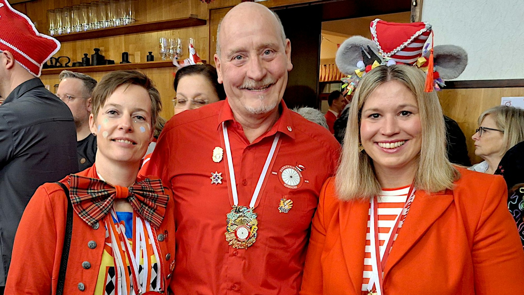 Annegret Lewak (l.), Rudi Huth und Jennifer Meuren lächeln in roten Karnevalsoutfits in die Kamera.
