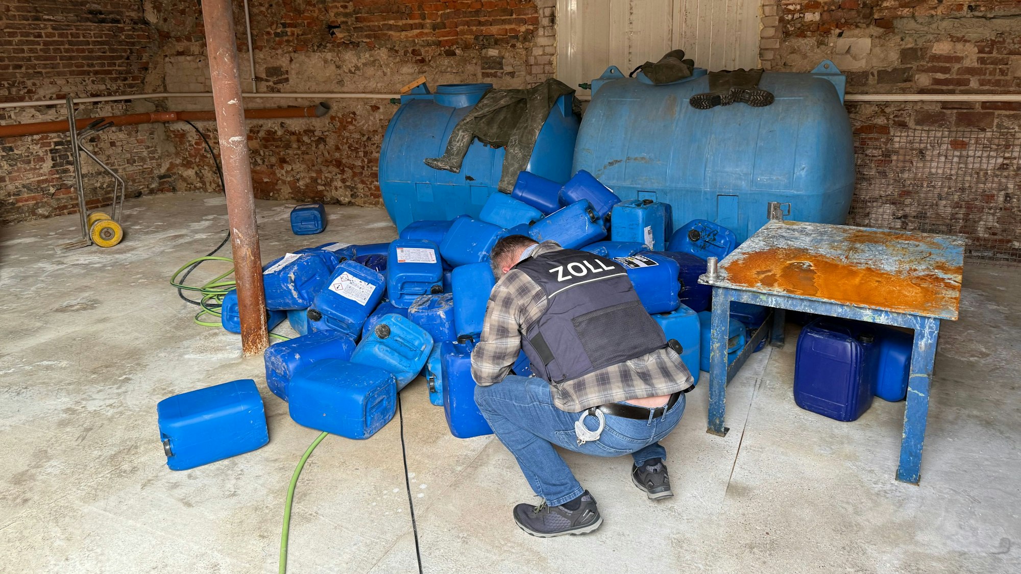 Ein Zollfahnder kniet vor blauen Kanistern.