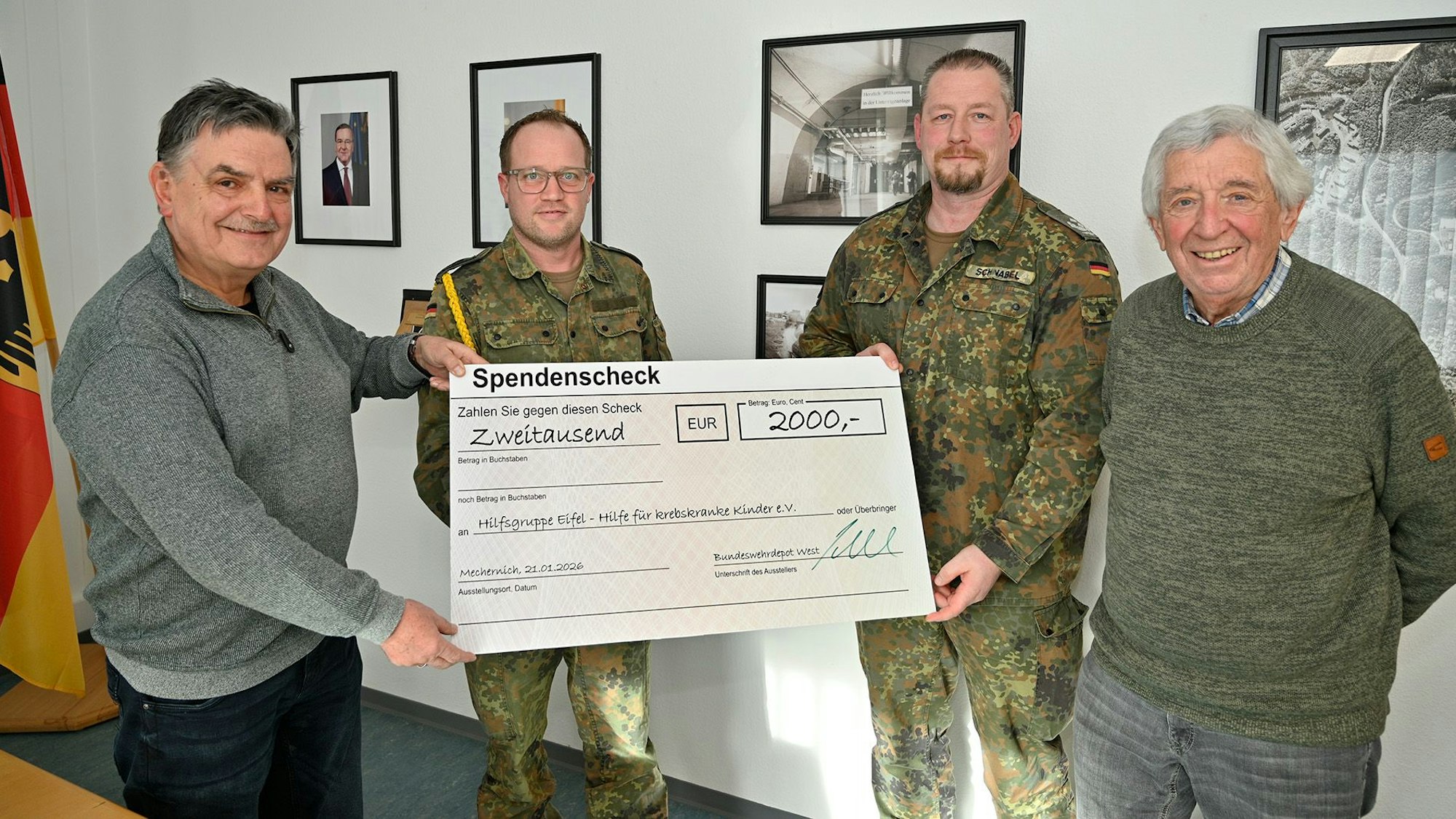 Zwei Bundeswehrangehörige in Tarnunifom überreichen einen Spendenscheck an zwei Zivilisten.