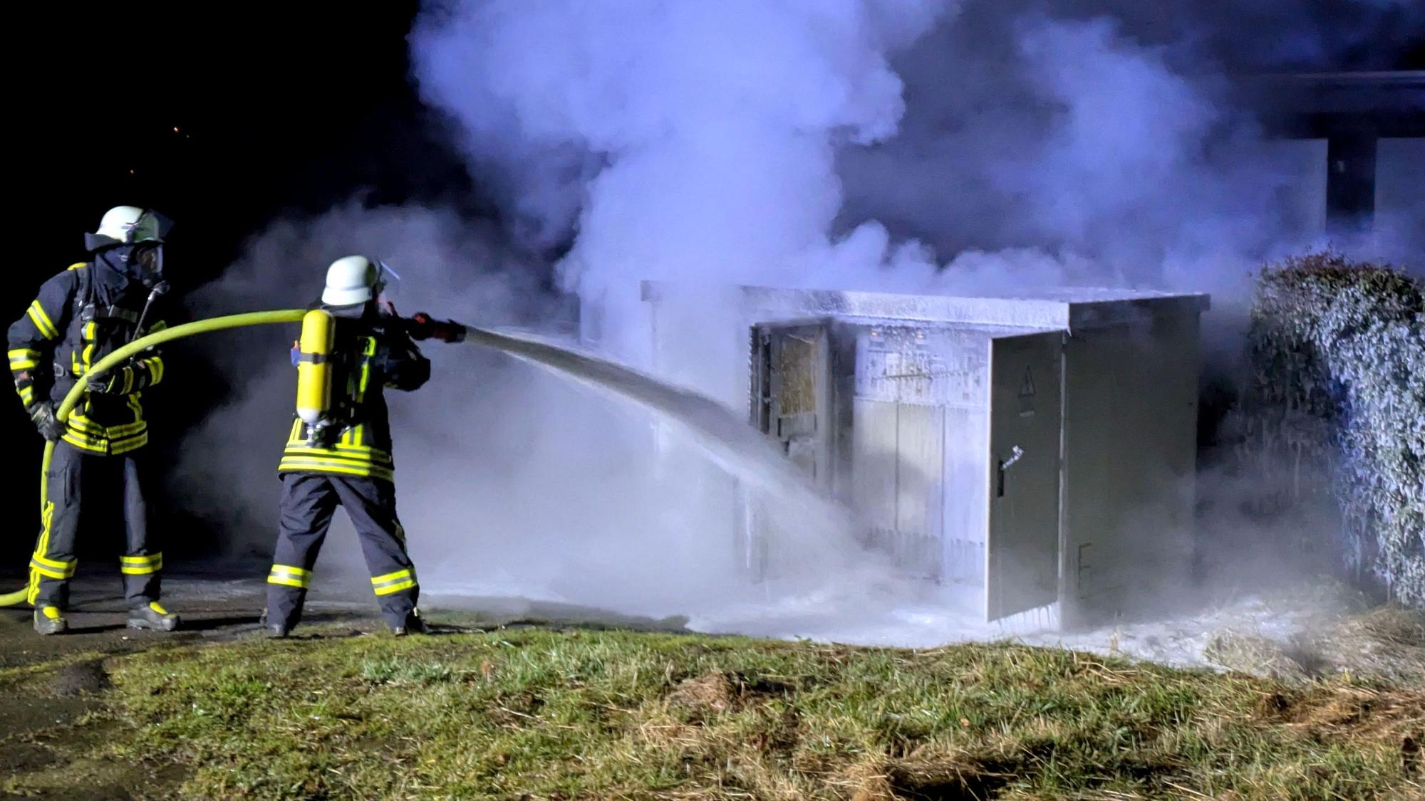 Zwei Feuerwehrleute löschen einen brennenden Trafo in der Bergstraße in Nettersheim mit Schaum.