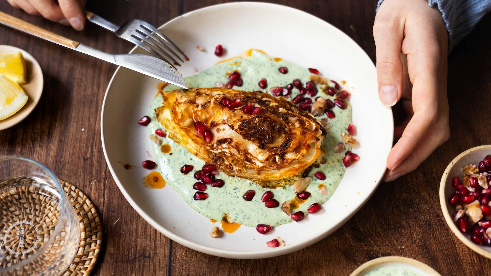 Die Spitzkohl-Viertel werden vor dem Backen kurz in der Pfanne angebraten. Nach 40 Minuten im Ofen werden sie auf Kräuterjoghurt gebettet und mit Granatapfelkernen und Walnüssen getoppt.
