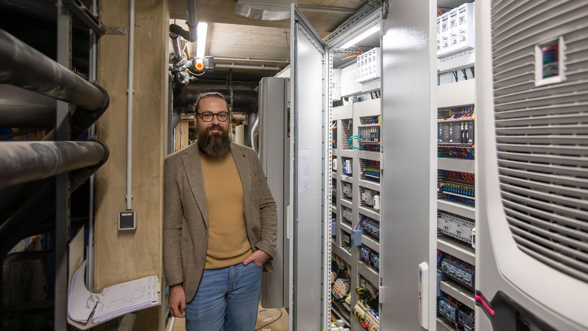 Ein Mann mit Vollbart steht in einem Raum voller Technik.