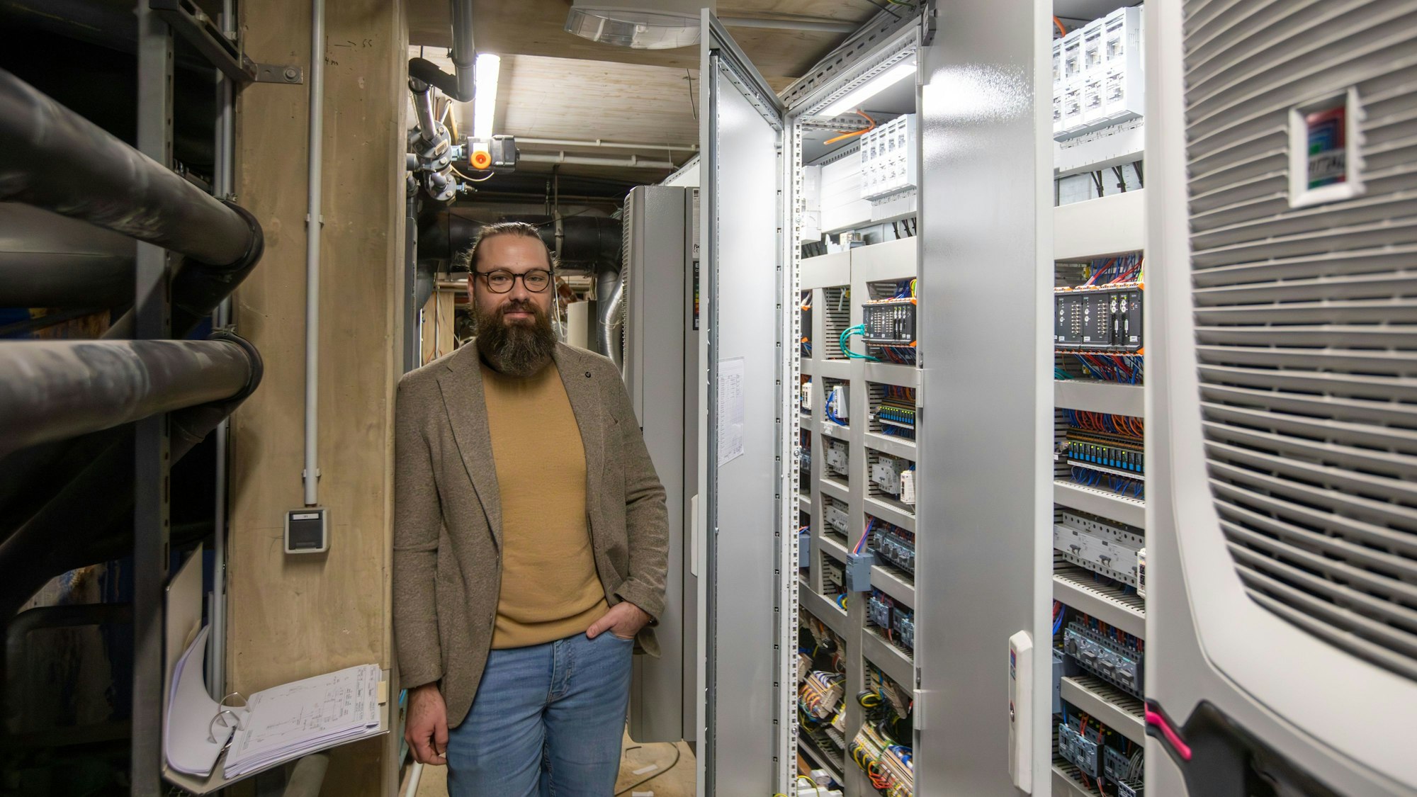 Ein Mann mit Vollbart steht in einem Raum voller Technik.