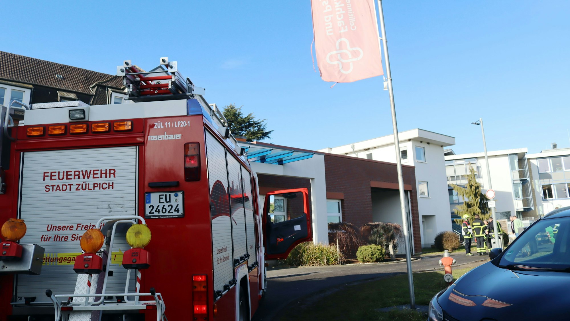 Ein Feuerwehrauto steht in der Einfahrt zu einer Fachklinik. Im Hintergrund sind Feuerwehrleute zu erkennen.