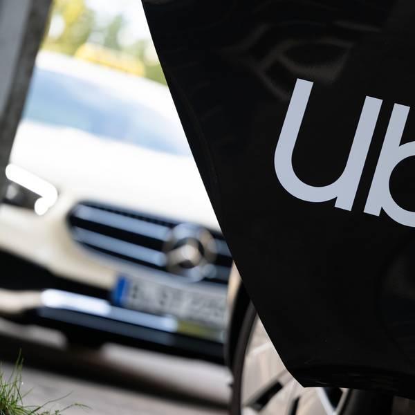 Ein Mietwagen mit einem Schriftzug des Fahrtenvermittlers Uber steht vor einem Taxi.